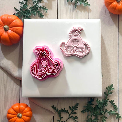 Planchette clay cutter and imprint side by side on white tile with pumpkins