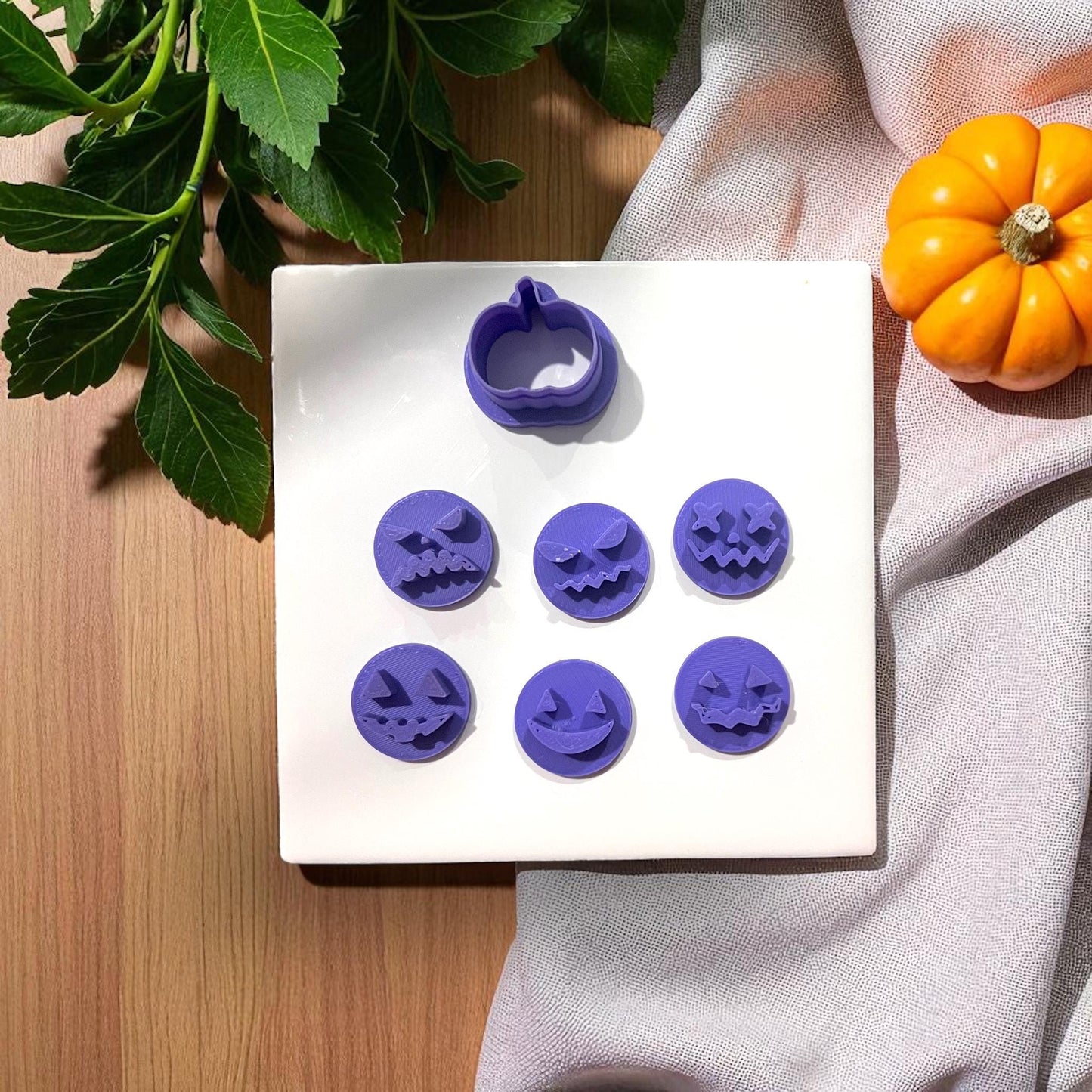 Purple pumpkin face clay cutters on white tile with pumpkins