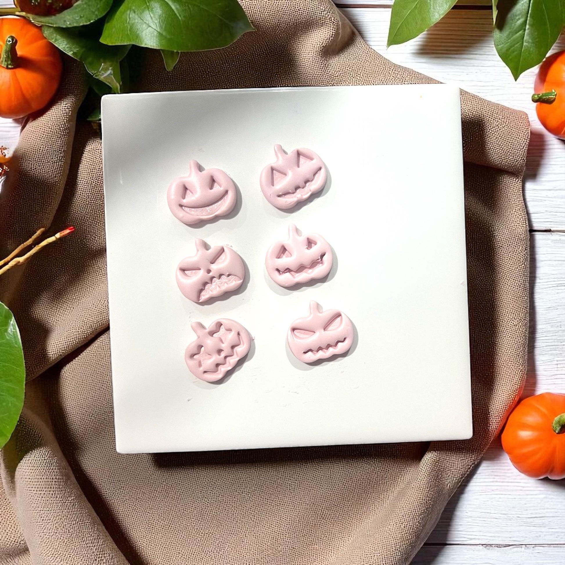 Pink pumpkin face clay shapes on white tile with pumpkins and leaves