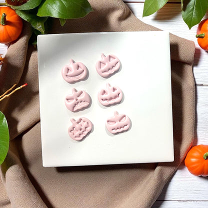 Pink pumpkin face clay shapes on white tile with pumpkins and leaves