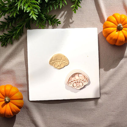 Mushroom skull clay cutter next to clay shape on white tile