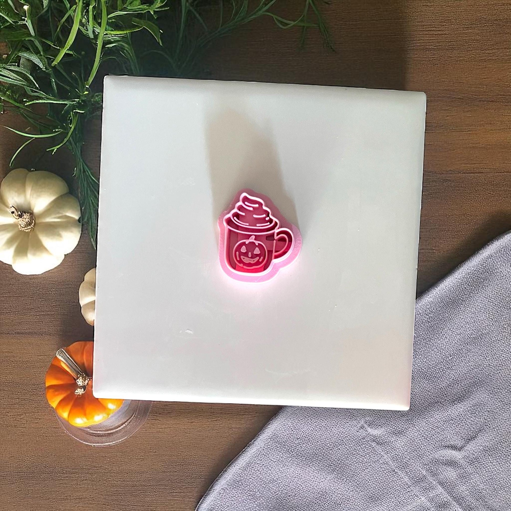 Pumpkin mug clay cutter and clay piece on white tile with greenery