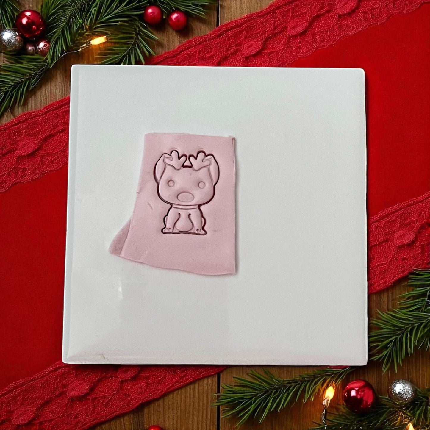 Pink clay imprint of dog with reindeer antlers on white tile with red ribbon