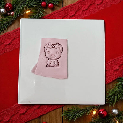 Pink clay imprint of dog with reindeer antlers on white tile with red ribbon