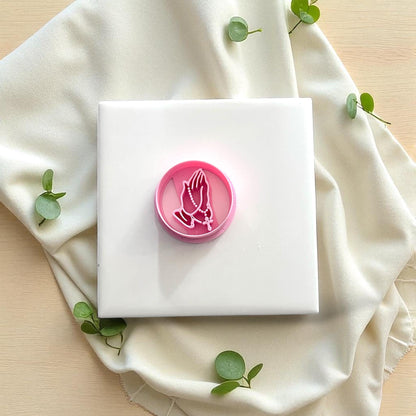 Pink praying hands with rosary clay cutter on white tile with greenery accents
