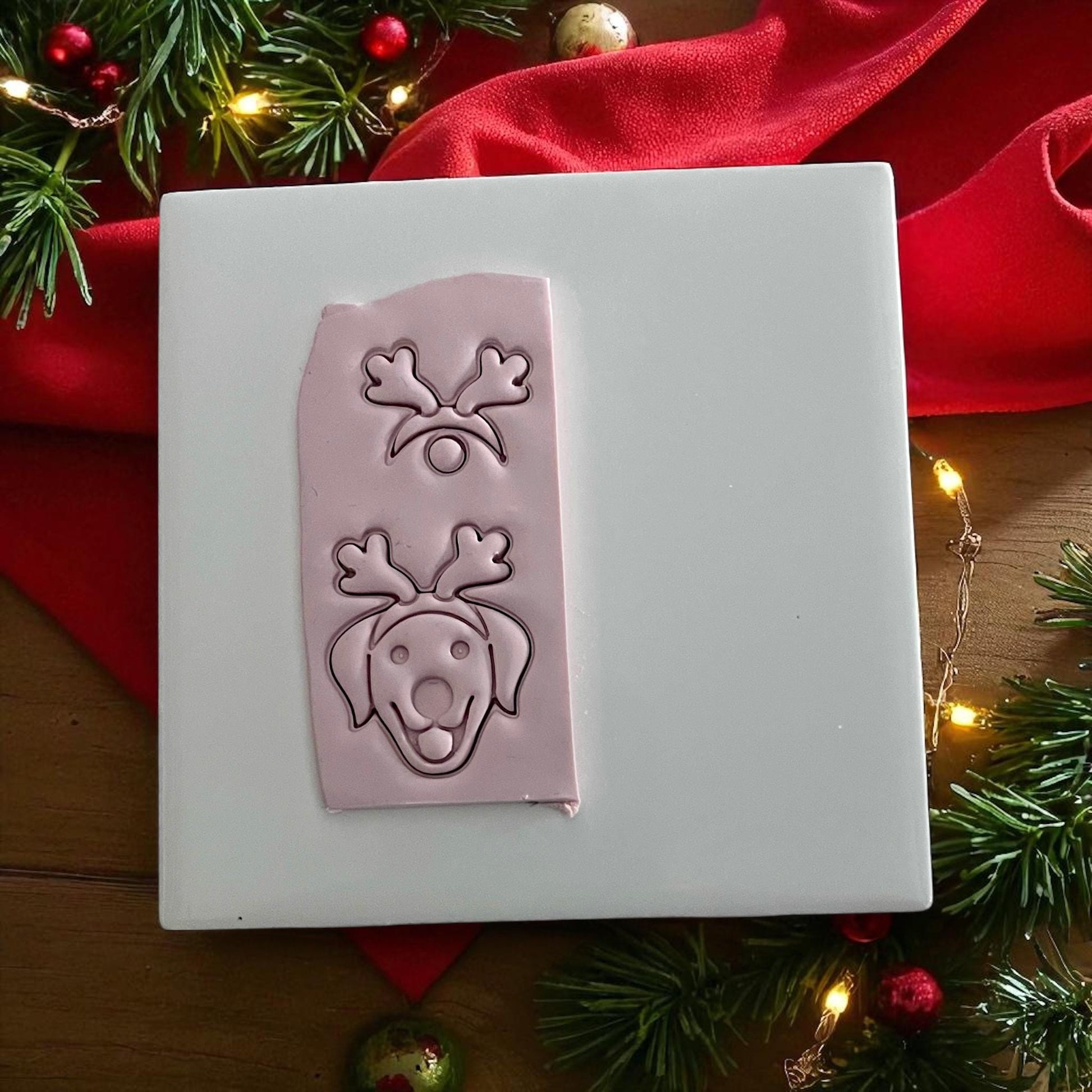Pink clay imprint of labrador with reindeer antlers and nose on white tile with red ribbon