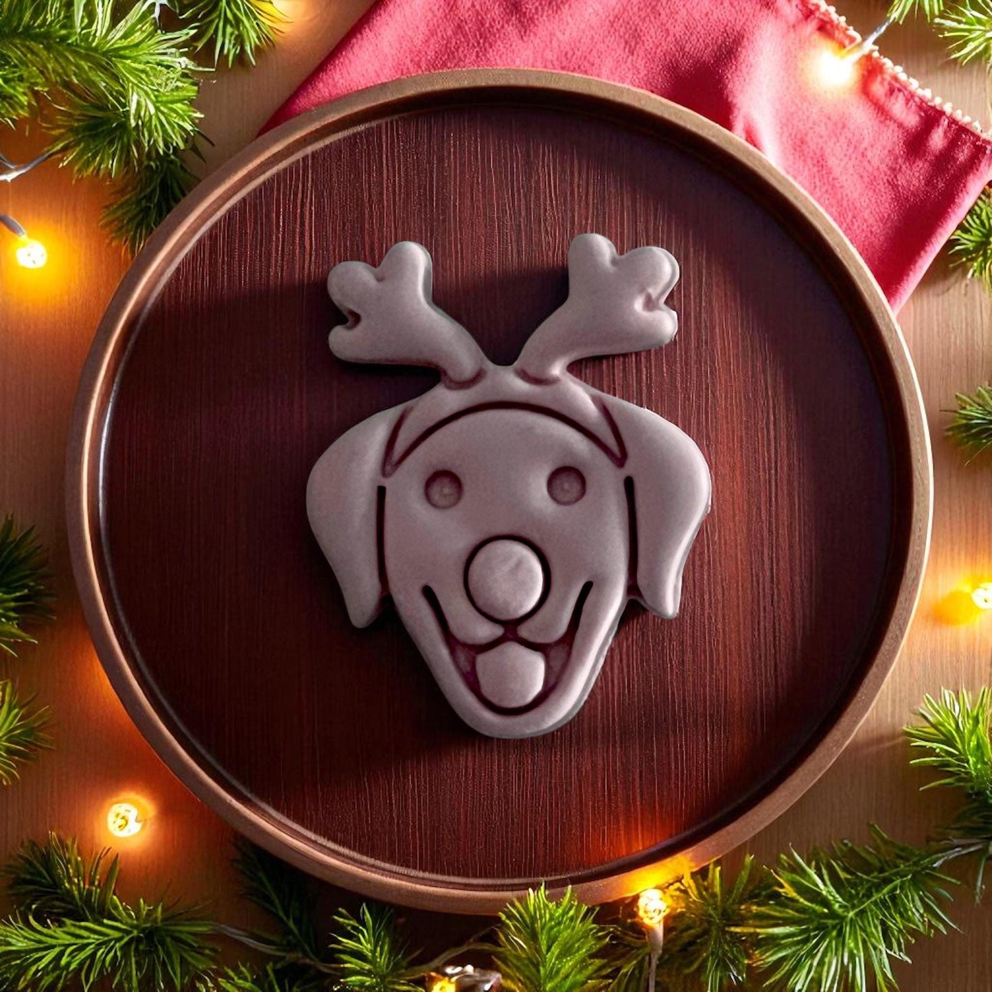 Large clay imprint of labrador with reindeer nose and antlers on wooden plate with Christmas greenery