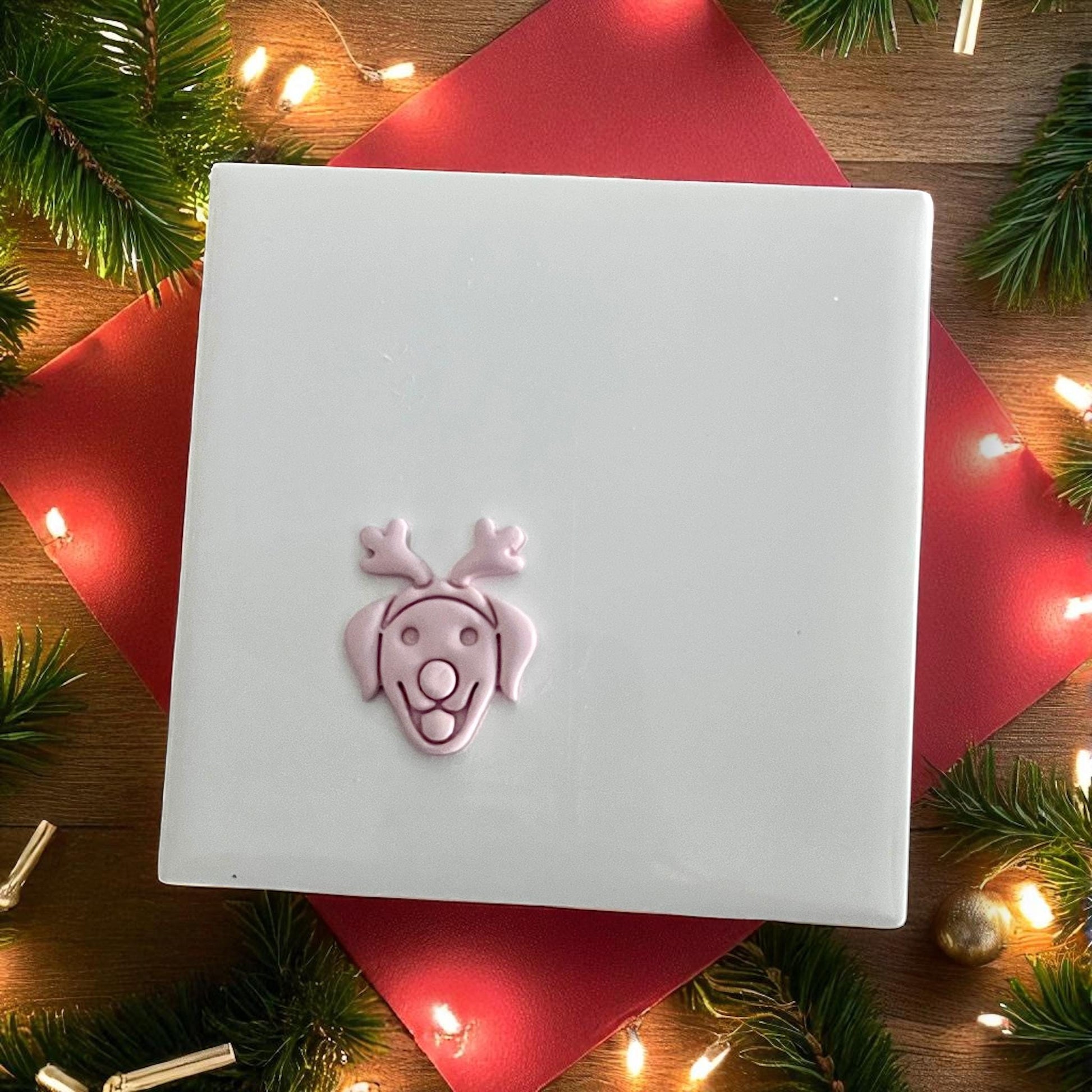 Small clay imprint of labrador with reindeer antlers displayed on white tile with holiday decor