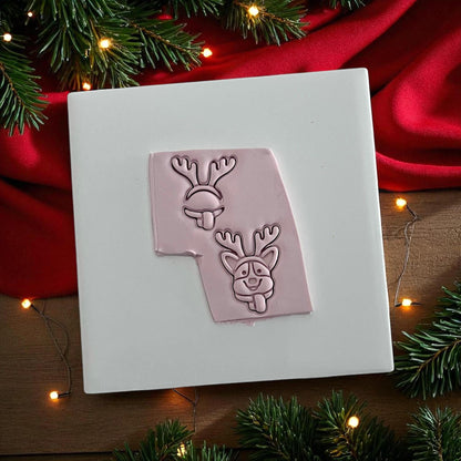 Pink clay imprint of corgi dog with reindeer antlers and tongue out on white tile with red cloth
