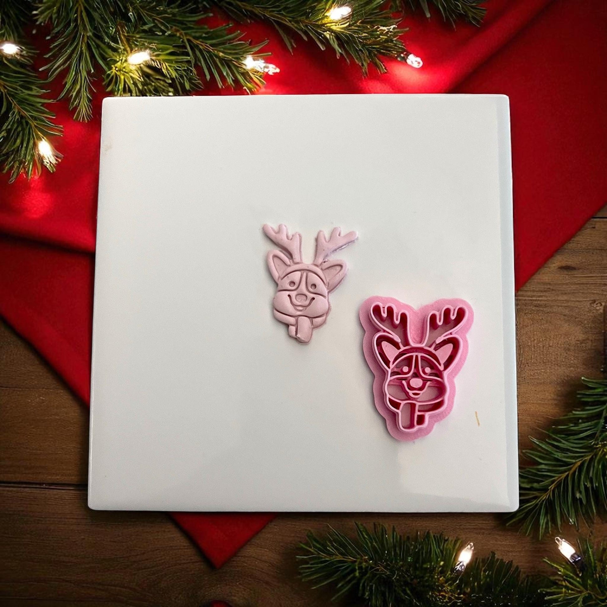 Pink clay imprint and cutter of corgi dog with reindeer antlers on white tile with lights