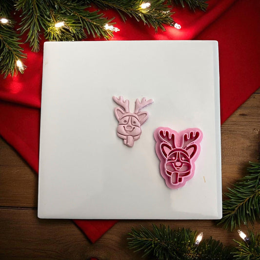 Pink clay imprint and cutter of corgi dog with reindeer antlers on white tile with lights