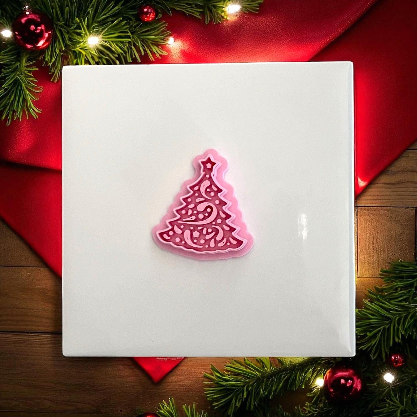 Pink Christmas tree polymer clay cutter on white tile with red holiday backdrop