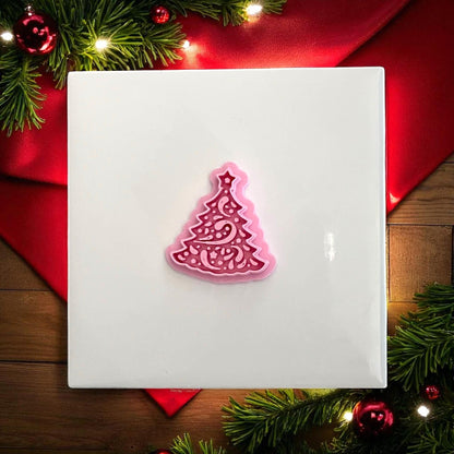 Pink Christmas tree polymer clay cutter on white tile with red holiday backdrop
