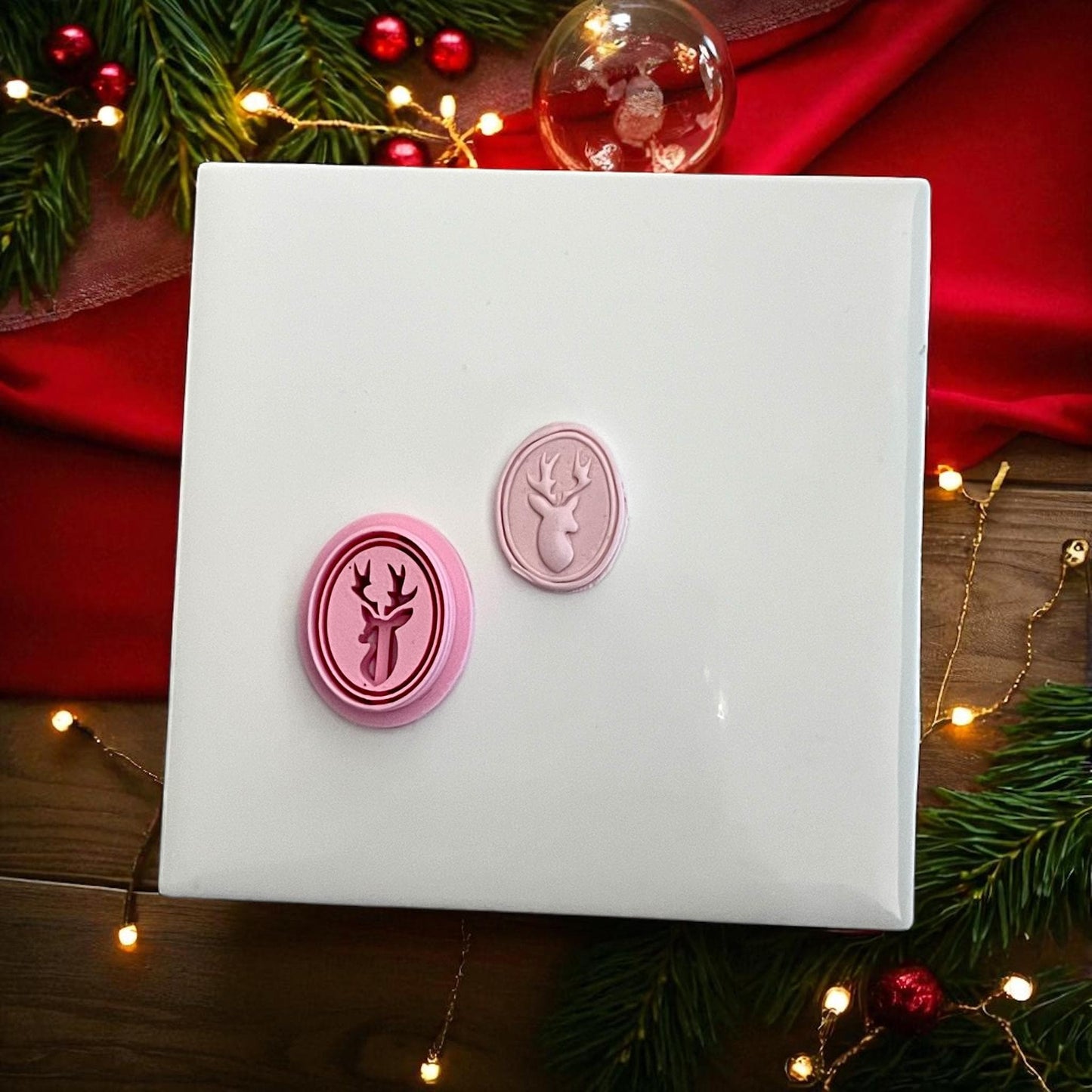 Oval reindeer clay imprint and pink cutter side by side on white tile with red ribbon
