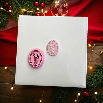 Oval reindeer clay imprint and pink cutter side by side on white tile with red ribbon