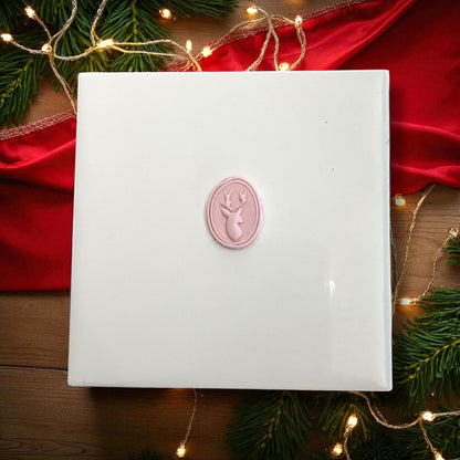 Small oval reindeer clay imprint with holiday lights and red ribbon backdrop