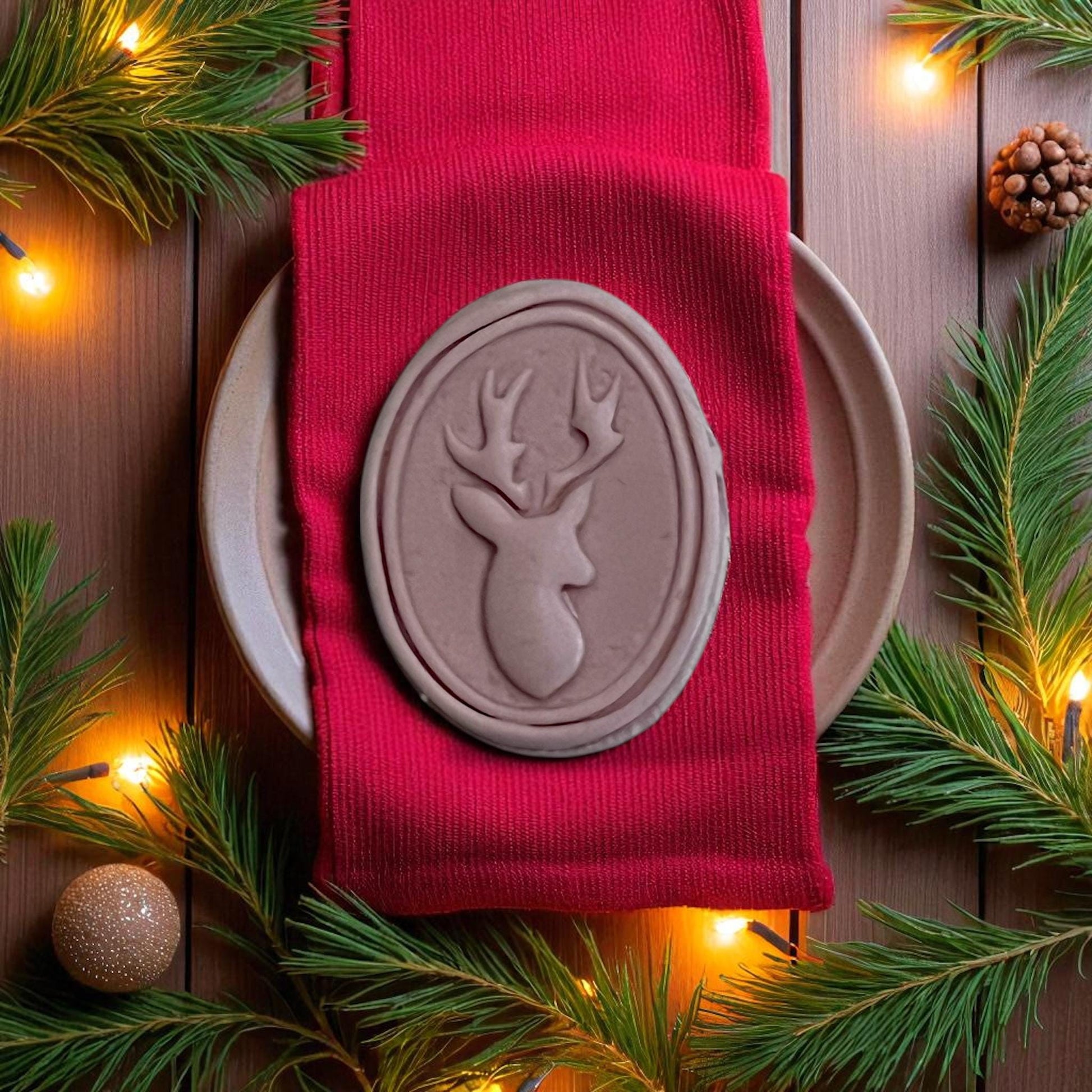 Large brown oval reindeer clay imprint on red napkin with Christmas lights and pine branches