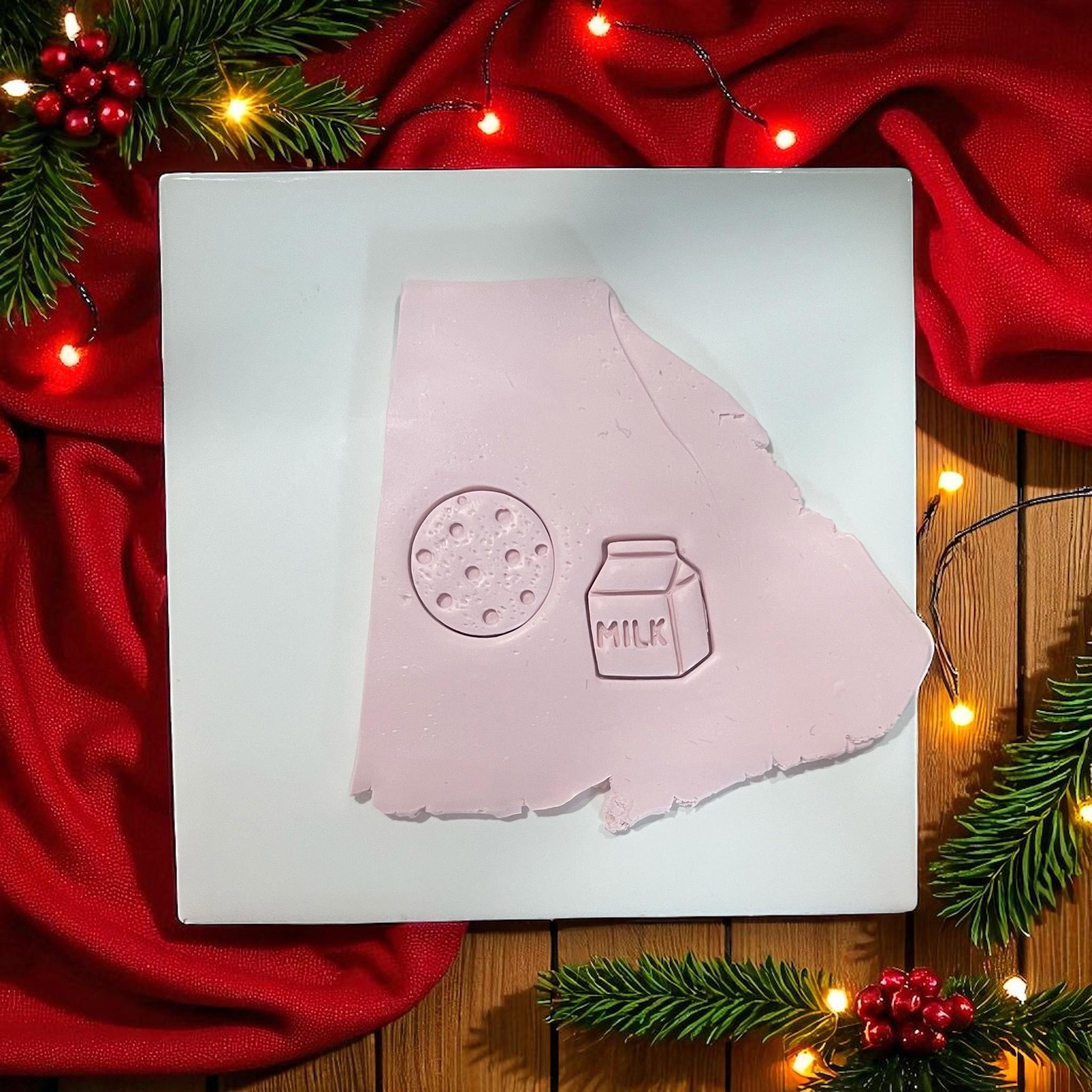 Milk carton and cookie clay imprints on pink clay slab with holiday lights