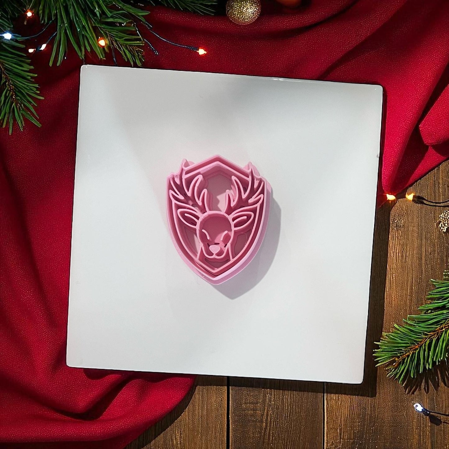 Pink reindeer polymer clay cutter on white background with red fabric