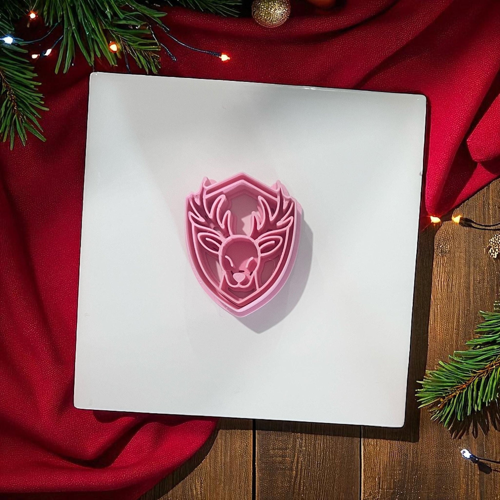 Pink reindeer polymer clay cutter on white background with red fabric