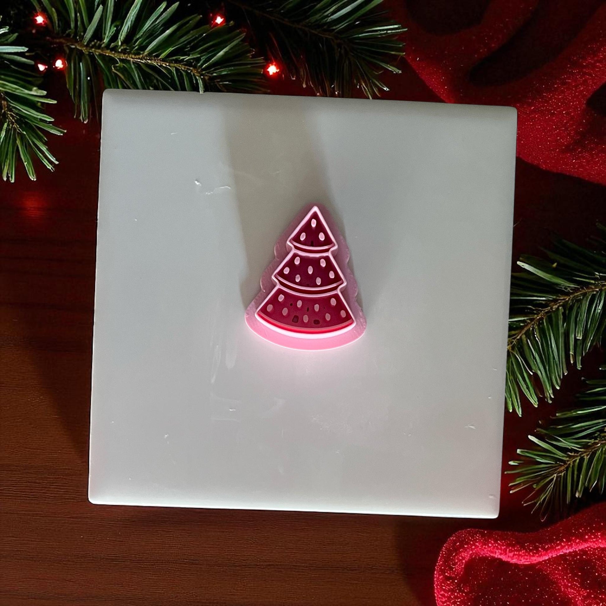 Pink watermelon Christmas tree clay cutter on white tile with holiday greenery