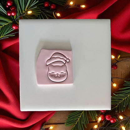 Santa kitty clay imprint on pink clay slab with lights and greenery
