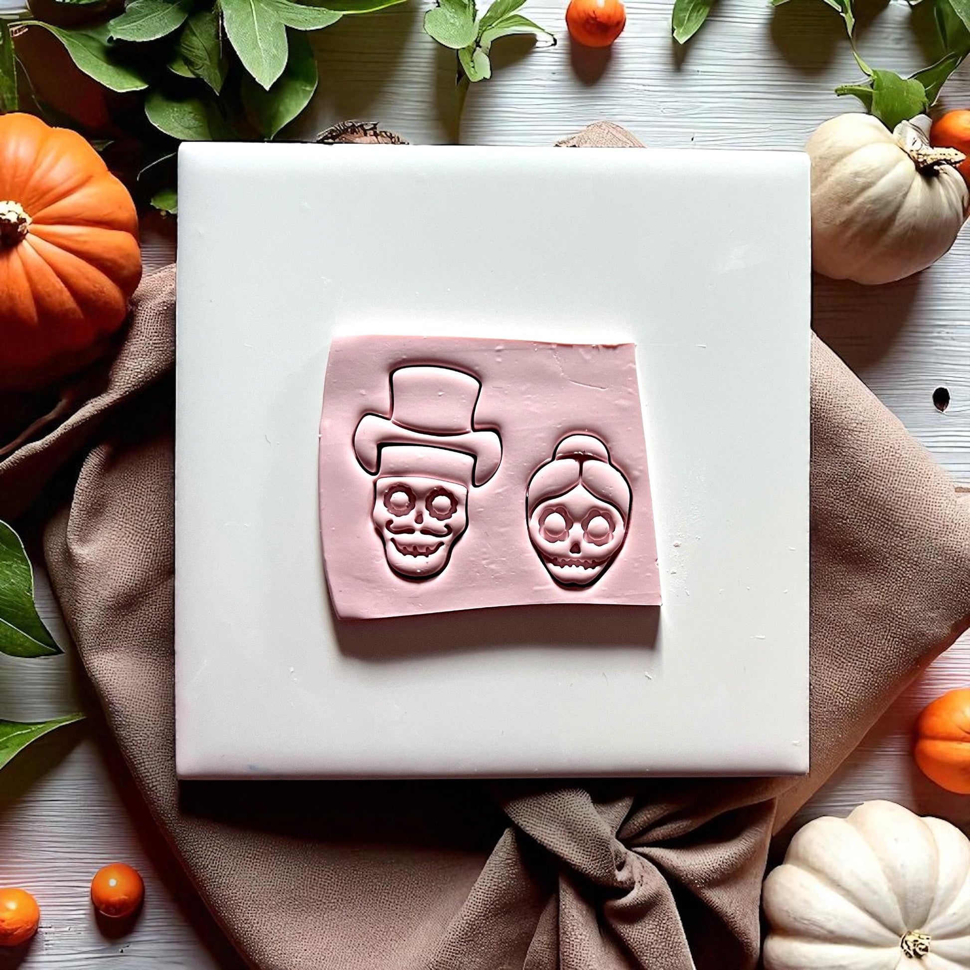 Bride and groom skull clay impressions on pink clay with pumpkins