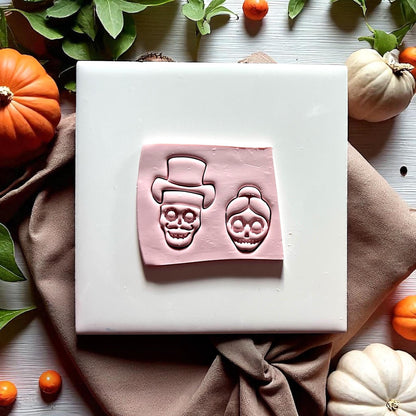 Bride and groom skull clay impressions on pink clay with pumpkins