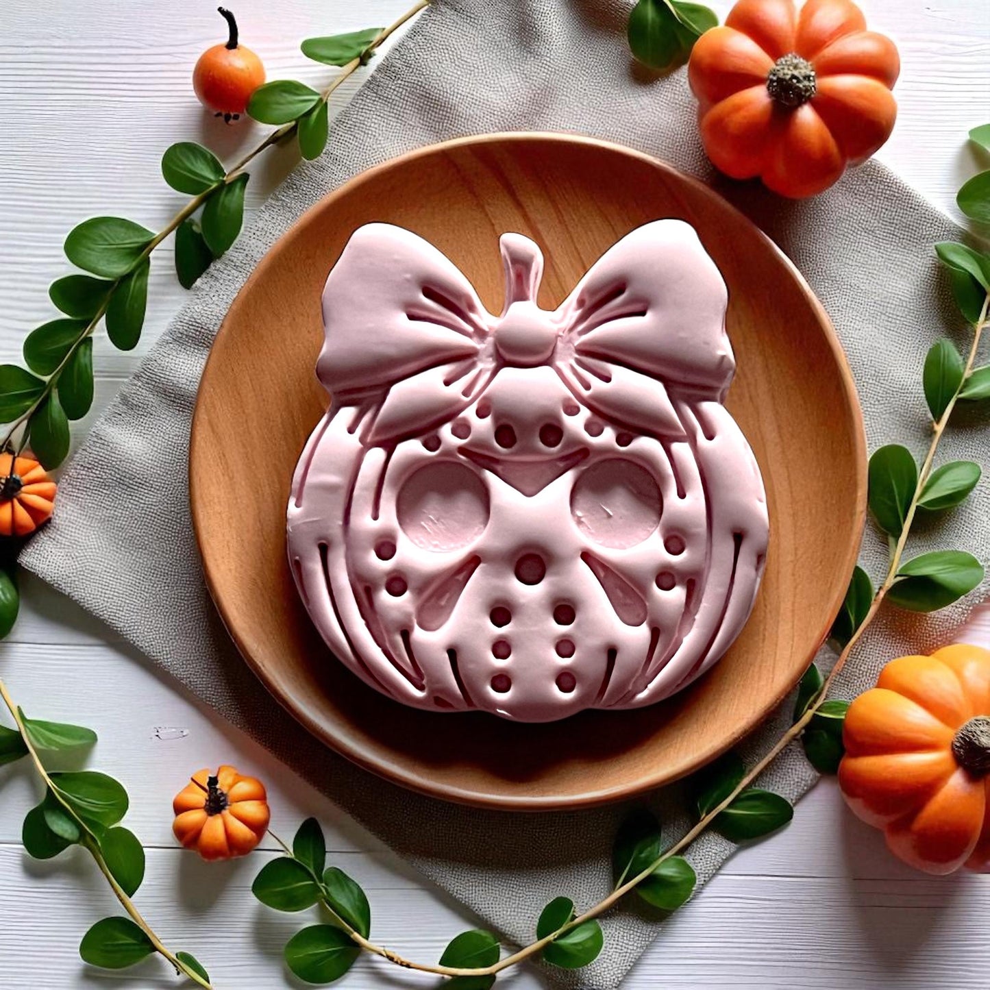 Large Jason mask pumpkin with coquette bow clay design on wooden plate with pumpkins