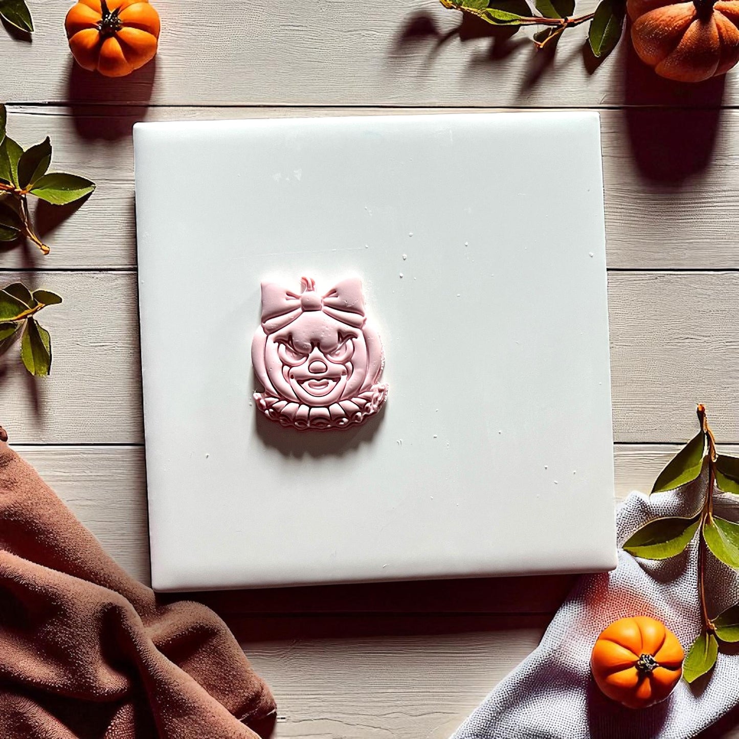 Pink clay clown pumpkin face with bow on white tile with pumpkins