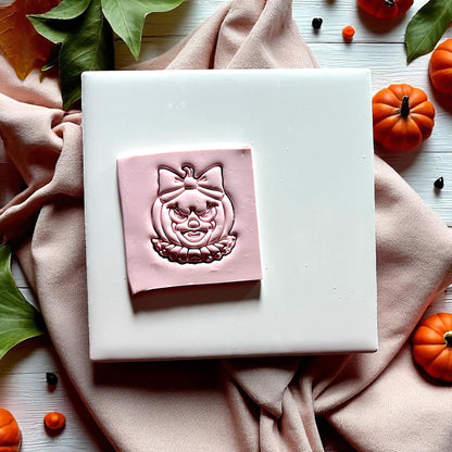 Clown pumpkin with bow clay cutter on white tile surrounded by pumpkins