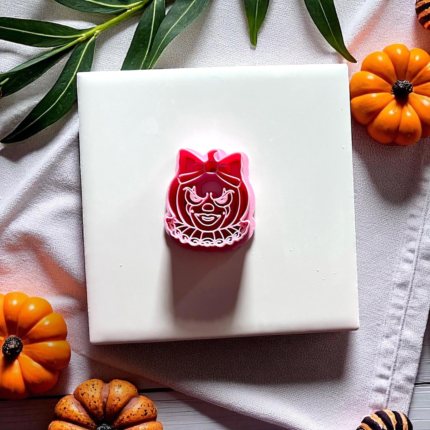 Clown pumpkin face imprint with bow on pink clay slab with pumpkins