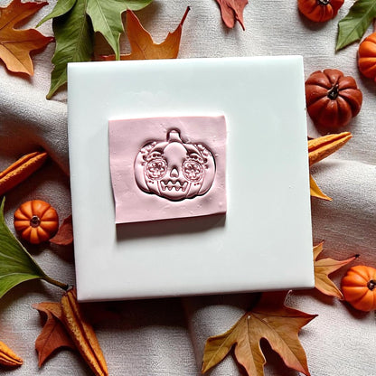 Pumpkin sugar skull clay cutter pressed into pink clay slab with autumn leaves