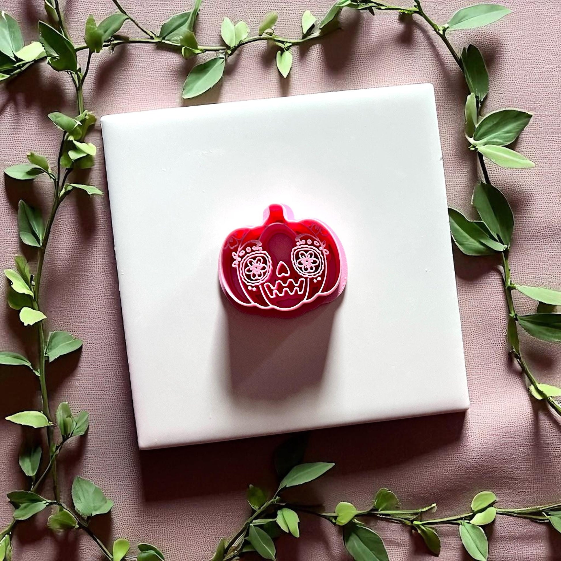 Sugar skull pumpkin clay cutter on white tile with green leaves border