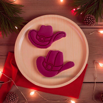 Two red clay cowboy hats displayed on wooden plate with holiday lights