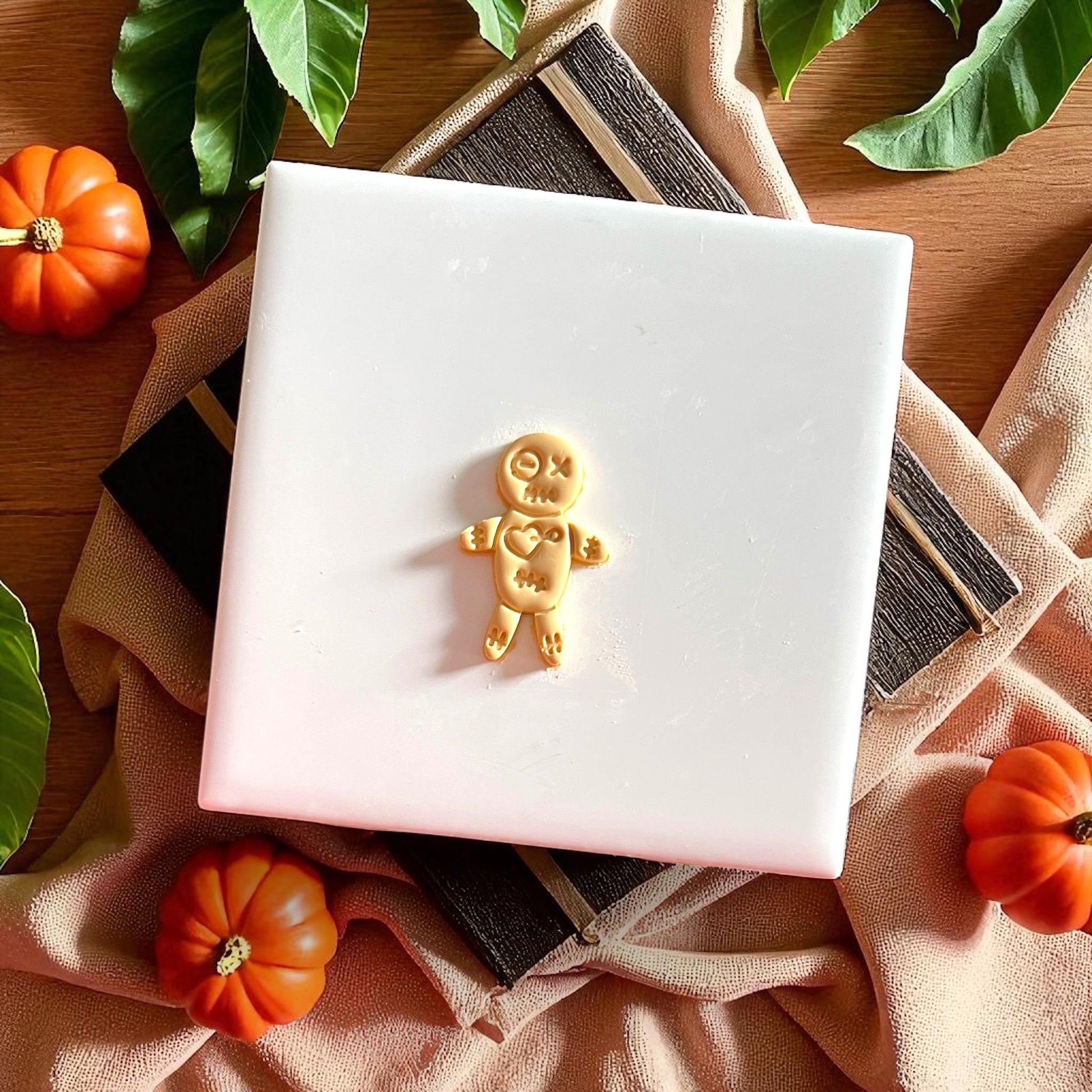 Yellow voodoo doll clay cutout on white tile with pumpkins and leaves