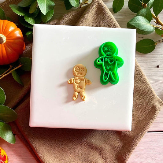 Green voodoo doll clay cutter with yellow clay cutout on white tile