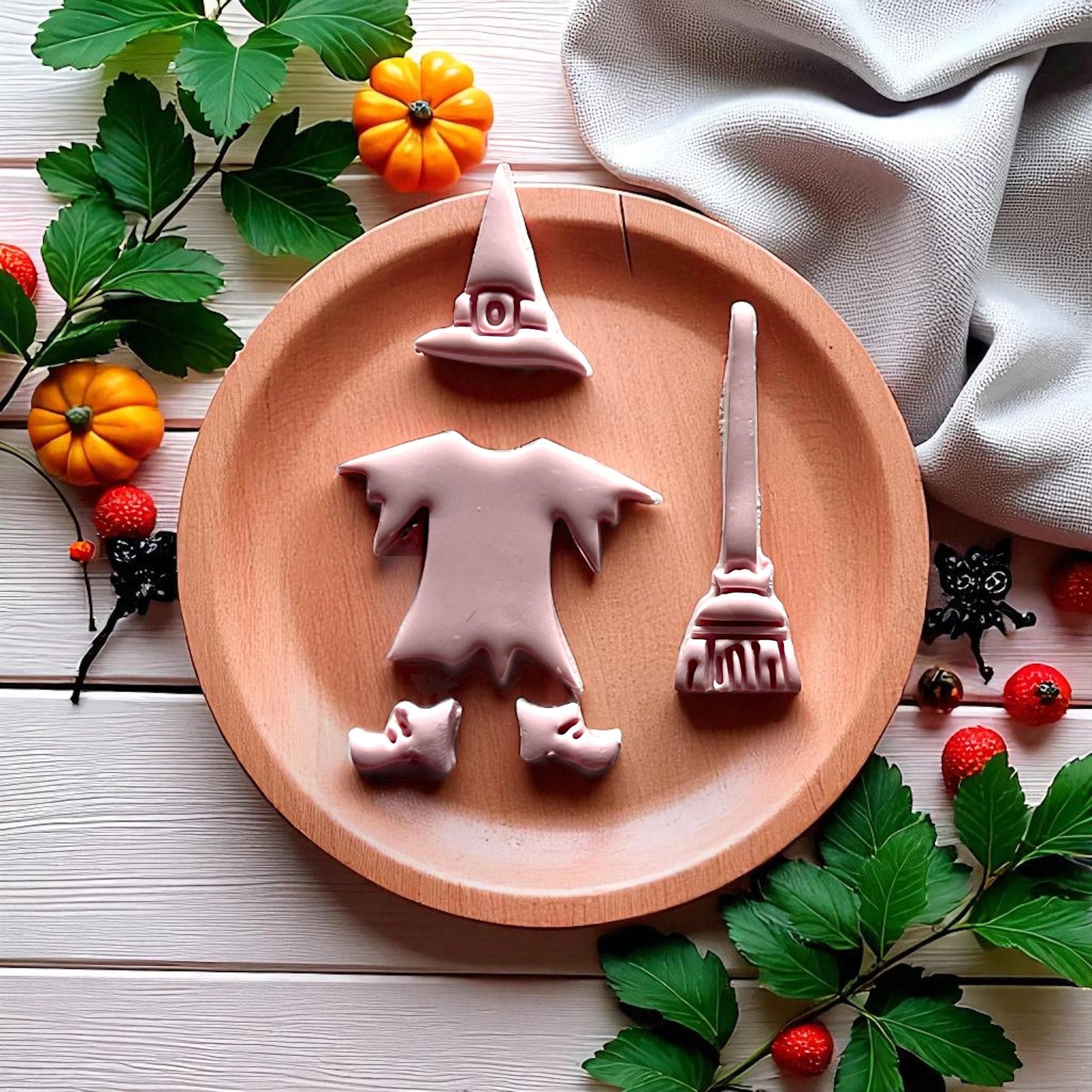 Pink witch clay cutouts of hat dress broom and shoes on round wooden plate