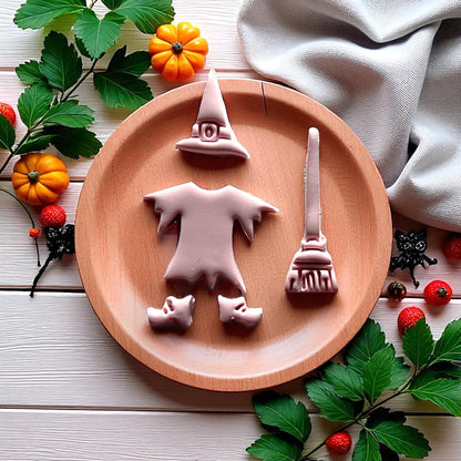 Pink witch clay cutouts of hat dress broom and shoes on round wooden plate
