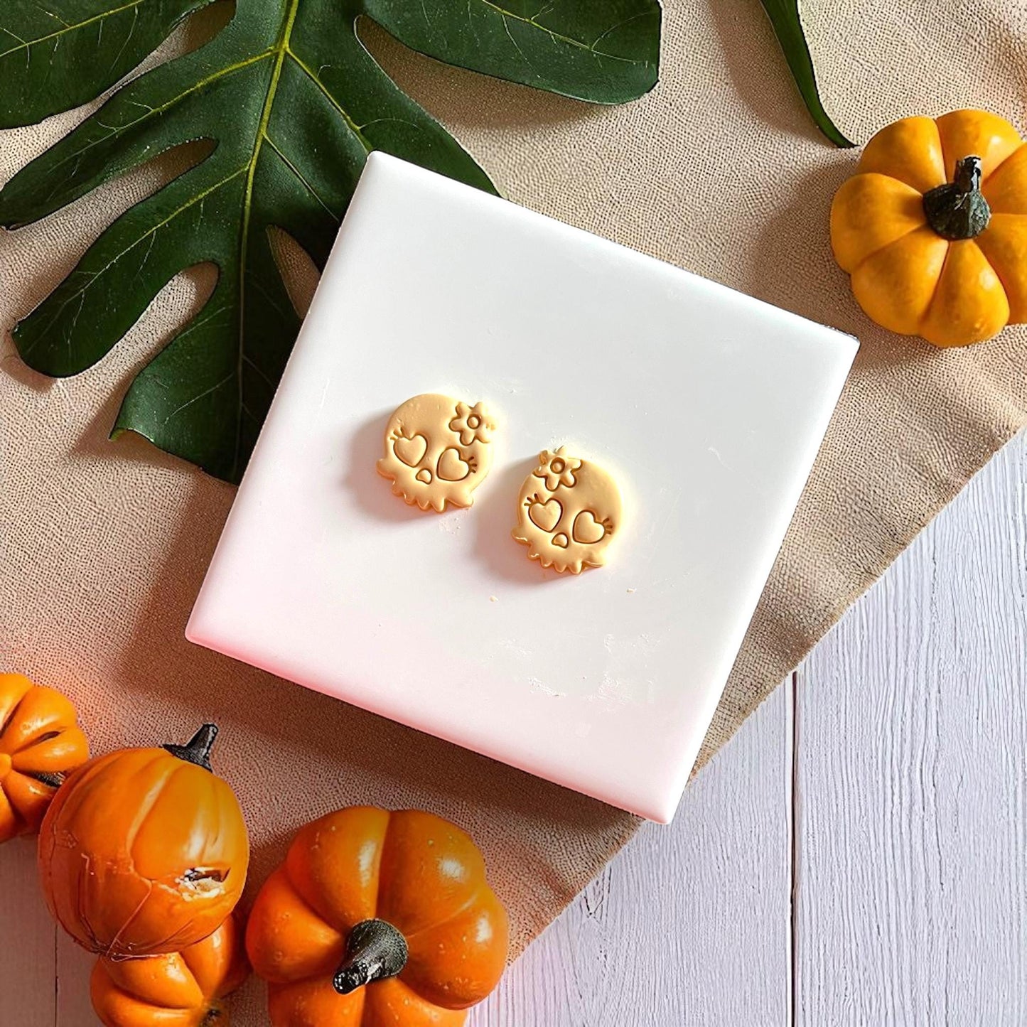 Small clay skull cutouts with heart eyes and flower detail on white tile