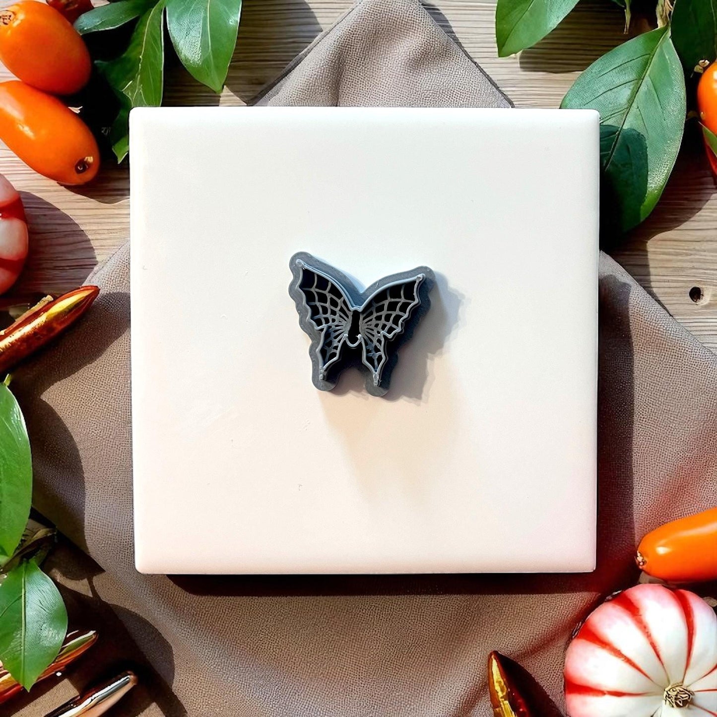 Gray spiderweb butterfly clay cutter on white tile with pumpkins