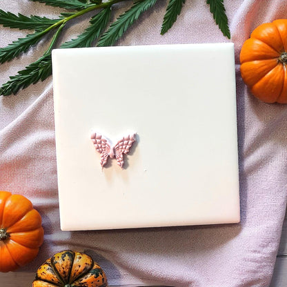 Small clay butterfly with web wings on white tile with pumpkins