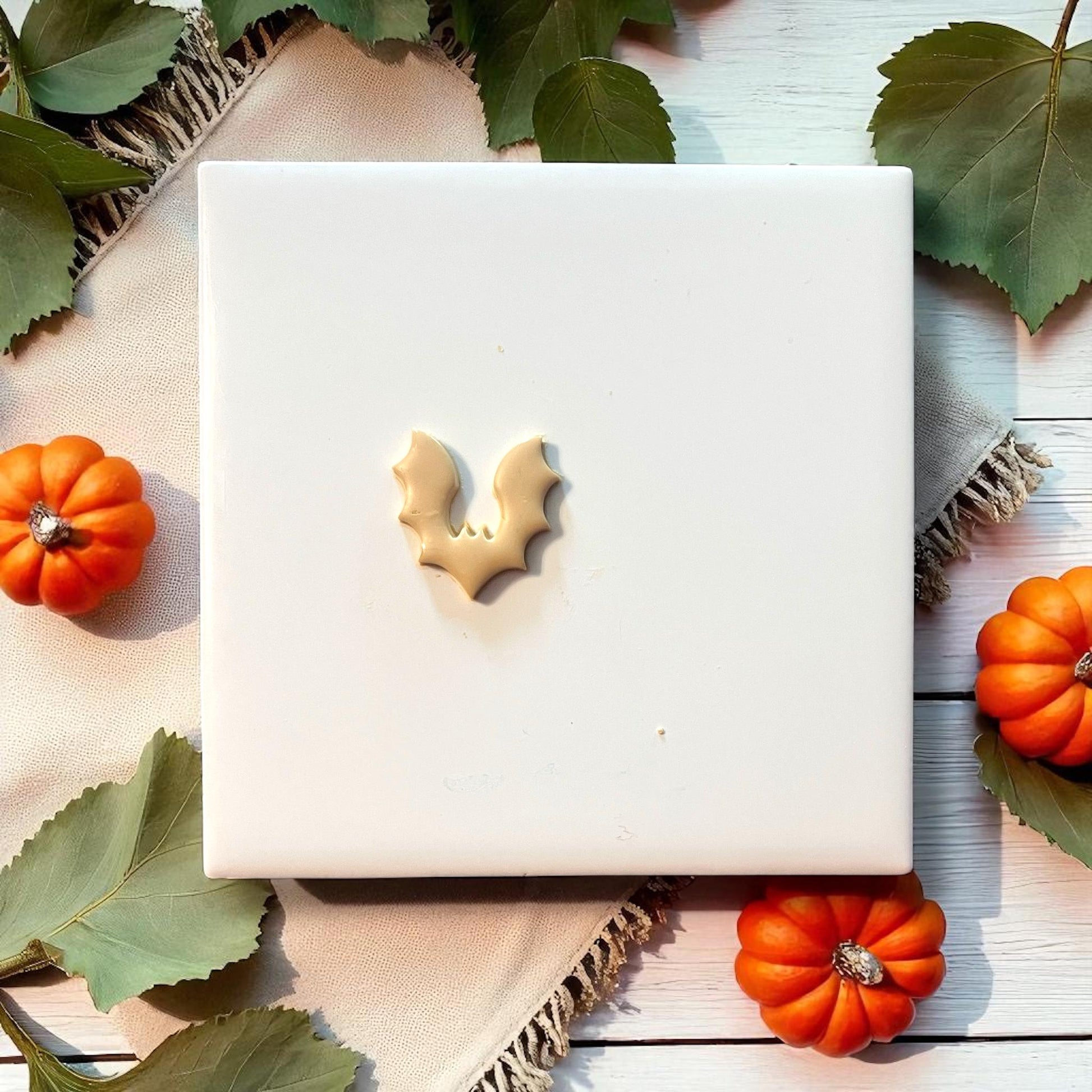 Small bat clay imprint on white tile with pumpkins and leaves