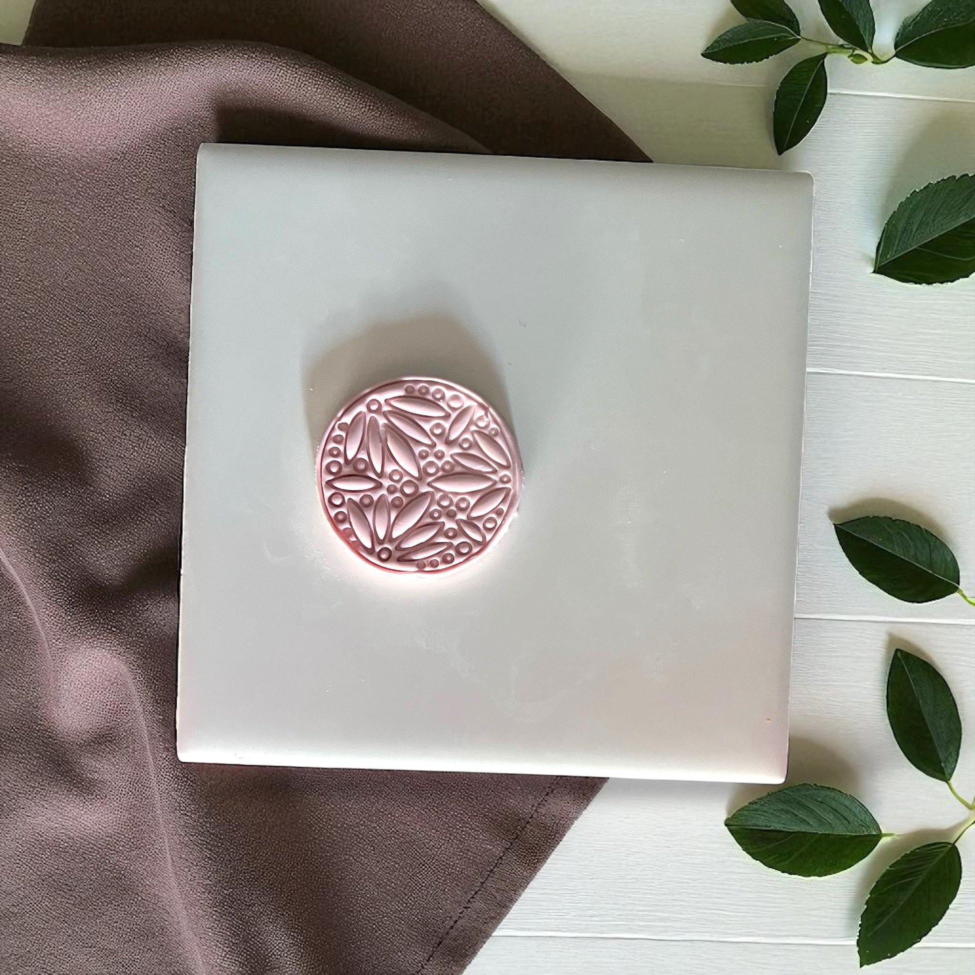 Small round botanical clay imprint with leafy pattern on white tile