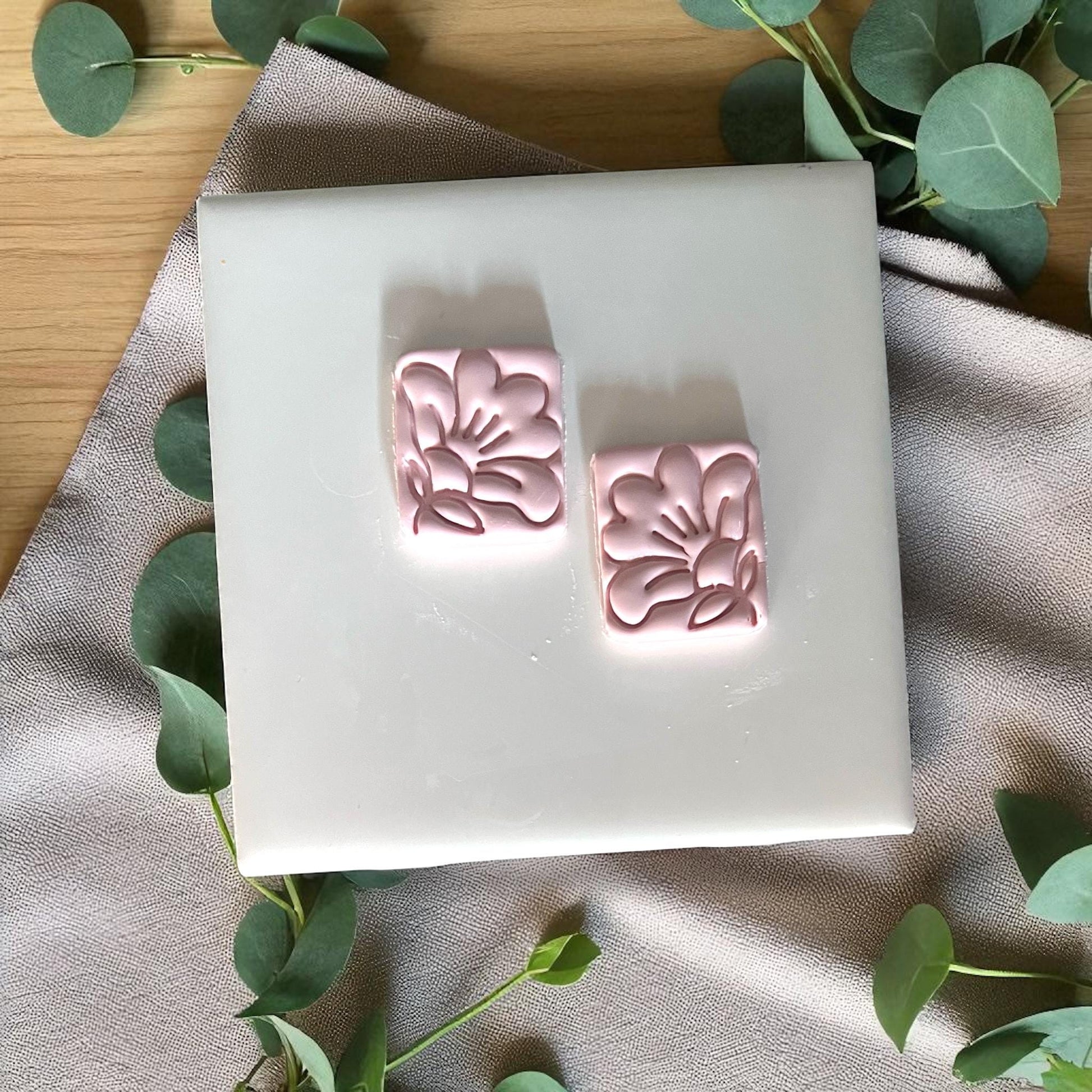 Two small square hibiscus floral clay imprints on white tile