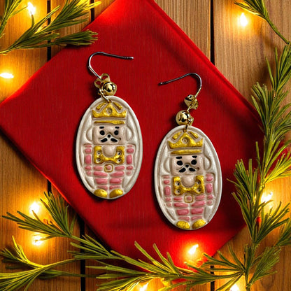 Close-up of finished nutcracker earrings with red and gold details surrounded by Christmas lights