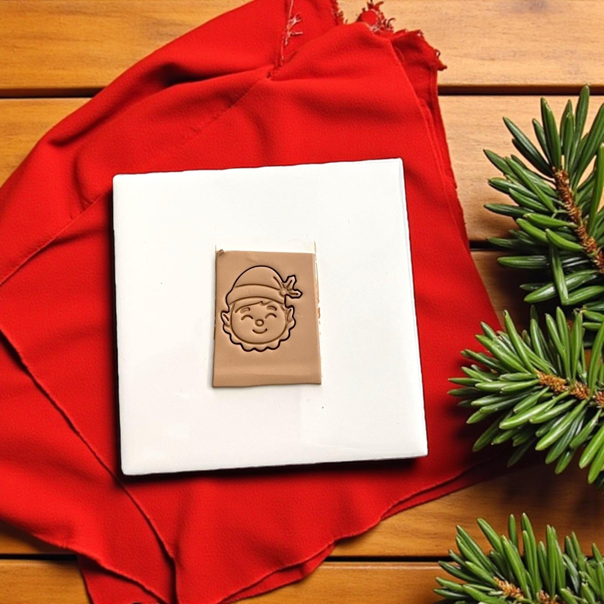 Happy elf polymer clay imprint on tan clay with red cloth background