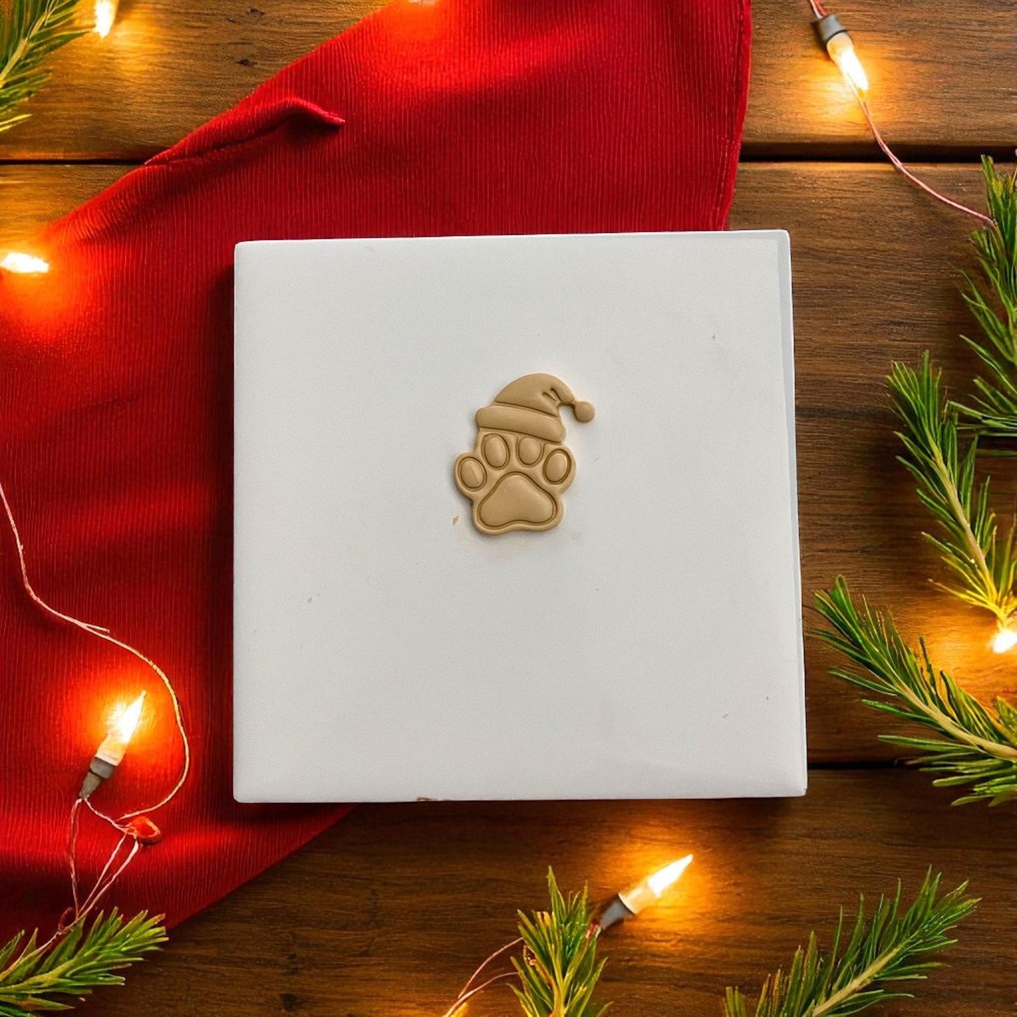 Christmas paw print polymer clay imprint with Santa hat on tan clay with festive lights
