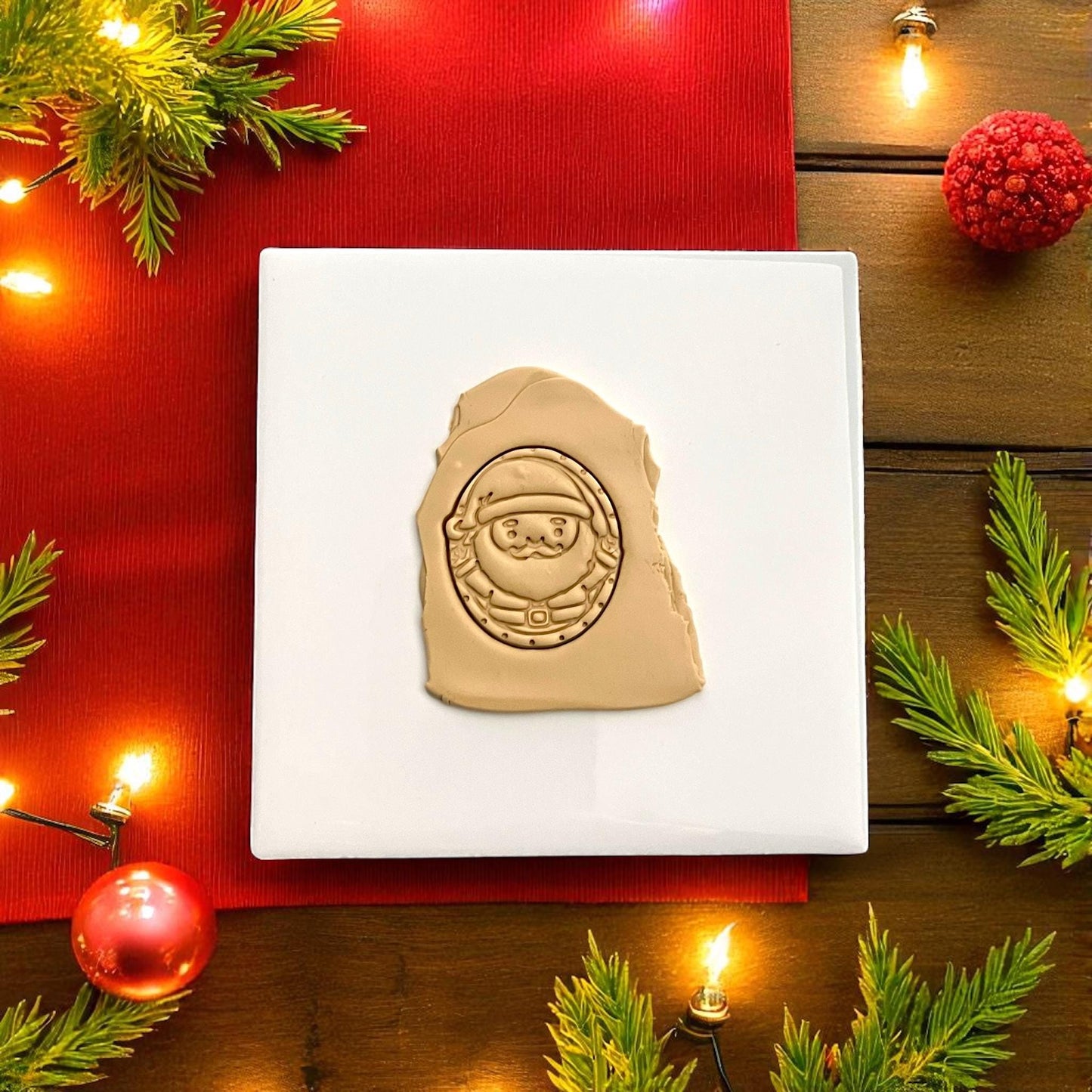 Santa face polymer clay imprint on tan clay with festive red background and lights