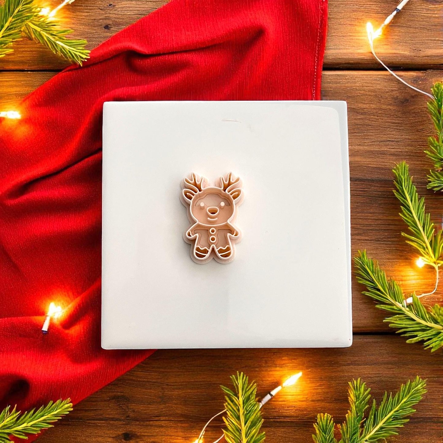 Gingerbread reindeer polymer clay cutter on red background surrounded by Christmas lights